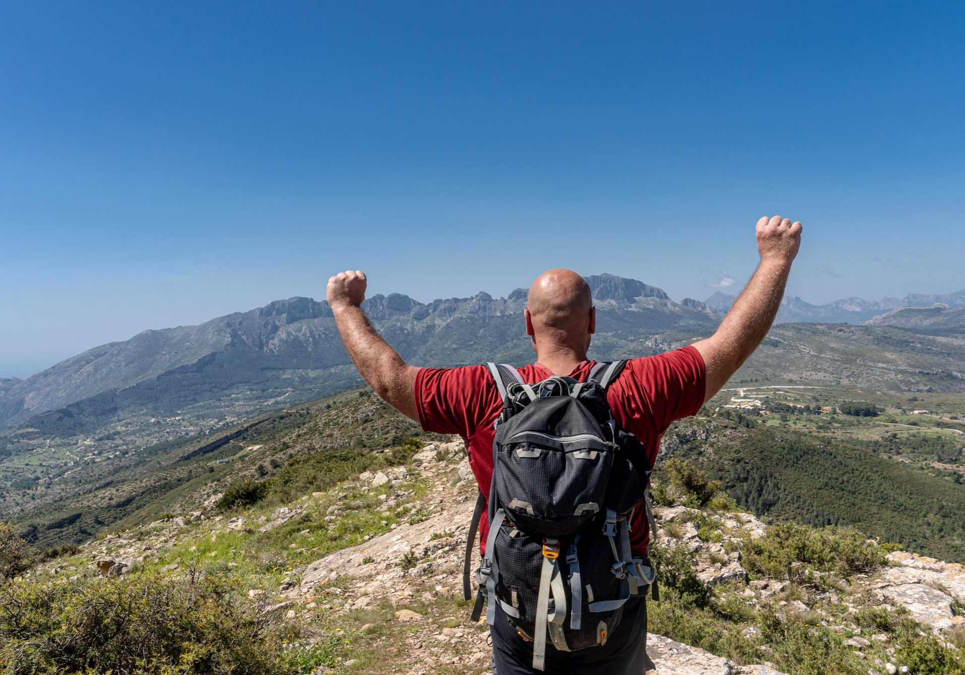 Rear view of a male hiker with his arms raised, with a gesture of happiness and success.
